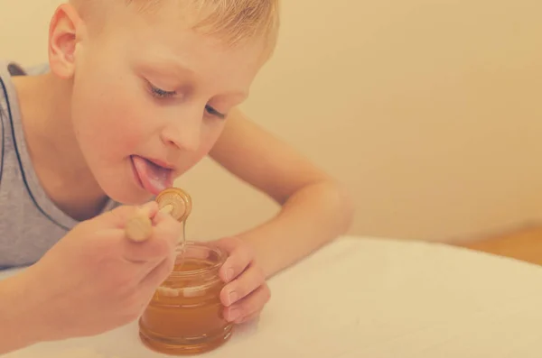 El chico que usa una cuchara para la miel se la come del frasco. . — Foto de Stock
