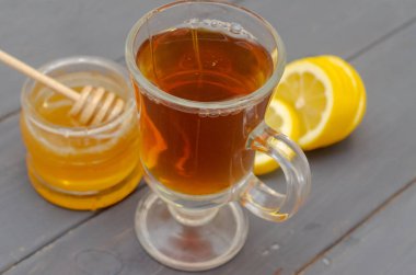 Bir fincan çay, dilimlenmiş limon ve bir kavanoz bal bileşimi.