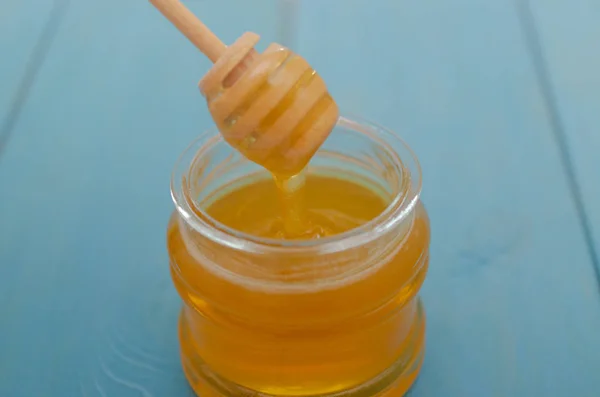 Honey and honey accessories for its use on a blue wooden background. — Stock Photo, Image