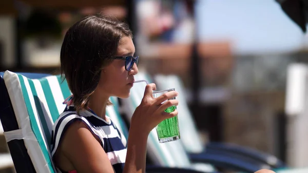girl is drinking soda lying on a lounger near a swimming pool