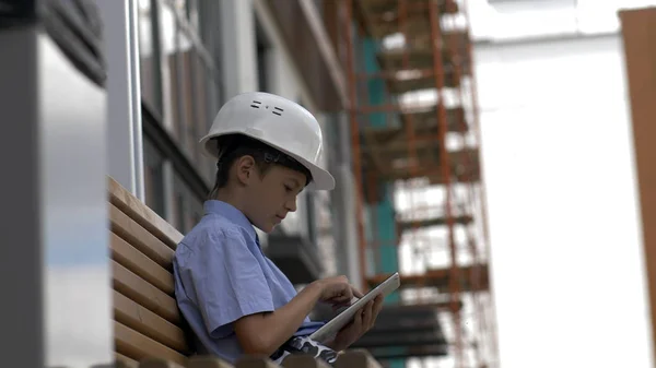 boy builder sits on the bench uses a tablet, monitors the builder project, plays a builder