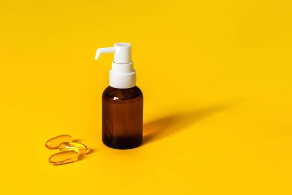 Kahverengi cam damlatıcı şişesi ve vitaminli üç kapsül ya da parlak sarı arka planda başka bir tıbbi tedavi. Sağlık sigortası konsepti. D vitamini, Omega 16, balık yağı. Kopyalama alanı