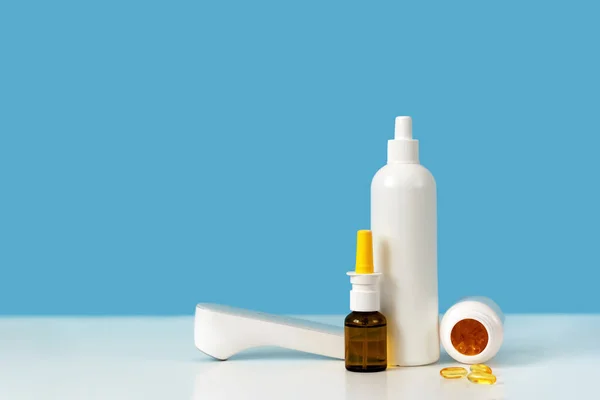 İlaç malzemeleri: termometre, beyaz plastik şişe, vitamin kapsülleri ve burun spreyi. Parlak mavi arka plan. Evde ilaç dolabı, bağışıklık koruma konsepti. Metin için alanı kopyala, kapat