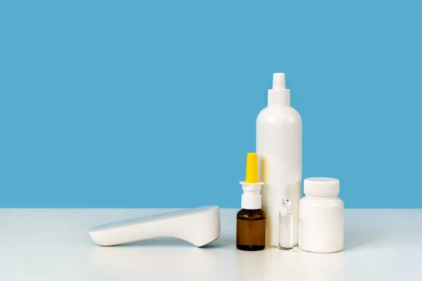 İlaç malzemeleri: termometre, beyaz plastik şişe, cam ampul ve burun spreyi. Parlak mavi arka plan. Grip veya eczane konsepti için ecza dolabı. Metin için alanı kopyala, kapat