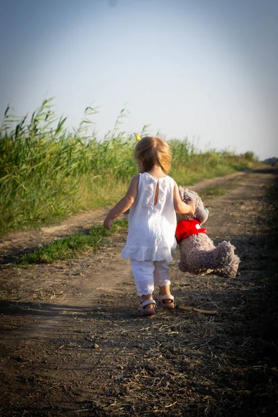 Ellerinde yumuşak bir oyuncak olan bir kız yola düşer. Beyaz takım elbiseli kız, yol kenarında sazlık.