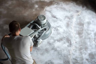 Construction worker in a family home living room that grind the concrete surface before applying epoxy flooring.Polyurethane and epoxy flooring.Concrete grinding. clipart