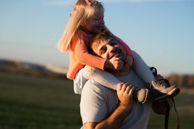 Mutlu baba oynuyor ve kızını omuzlarında taşıyor..
