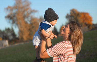 Açık havada mutlu ve uyumlu bir aile. Anne bebeği kusuyor, gülüyor ve yazın doğada oynuyor.