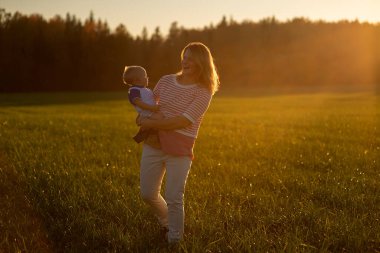 Açık havada mutlu ve uyumlu bir aile. Anne bebeği kusuyor, gülüyor ve yazın doğada oynuyor.