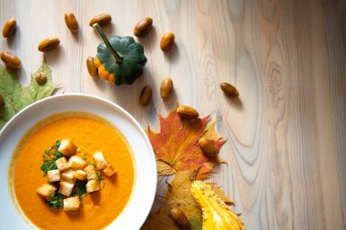 Sonbahar renklerinde kremalı ve krakerli ev yapımı balkabağı çorbası. Renkli yapraklar, balkabakları ve meşe palamudu ile süslenmiş. Şükran Günü yemeği.