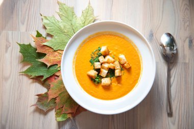Sonbahar renklerinde kremalı ve krakerli ev yapımı balkabağı çorbası. Renkli yapraklar, balkabakları ve meşe palamudu ile süslenmiş. Şükran Günü yemeği.