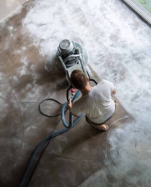 Construction worker in a family home living room that grind the concrete surface before applying epoxy flooring.Polyurethane and epoxy flooring.Concrete grinding. clipart