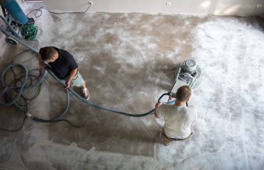 Construction worker in a family home living room that grind the concrete surface before applying epoxy flooring.Polyurethane and epoxy flooring.Concrete grinding. clipart