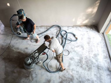 Construction worker in a family home living room that grind the concrete surface before applying epoxy flooring.Polyurethane and epoxy flooring.Concrete grinding. clipart