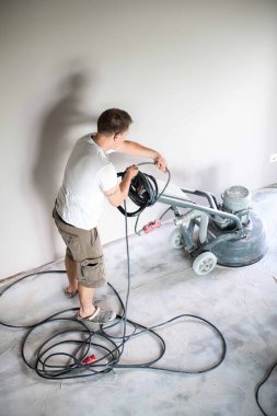 Construction worker in a family home living room that grind the concrete surface before applying epoxy flooring.Polyurethane and epoxy flooring.Concrete grinding. clipart