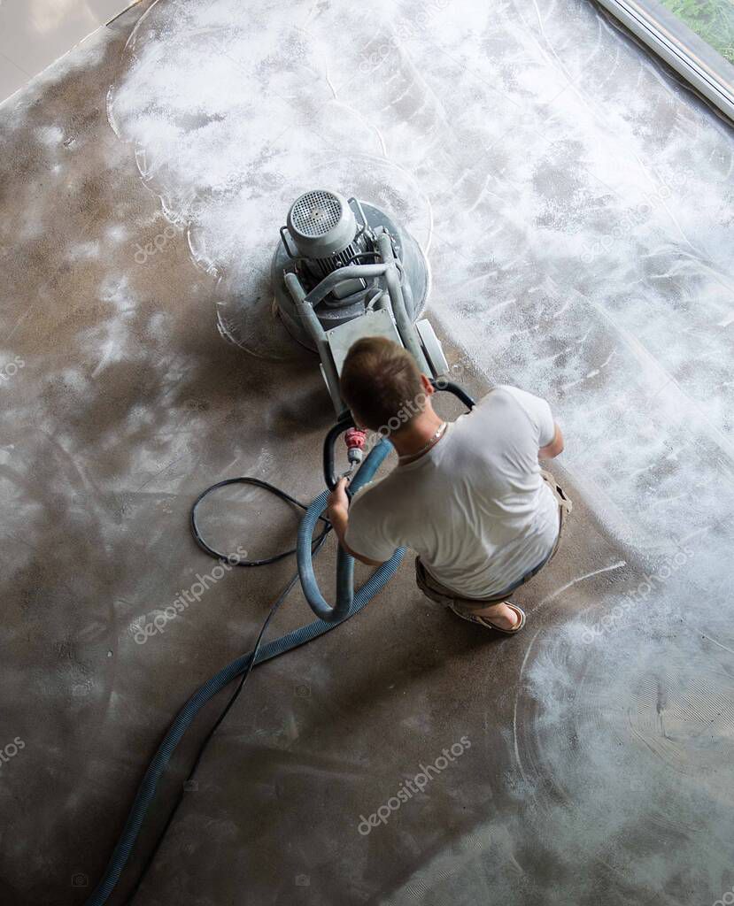 Construction worker in a family home living room that grind the concrete surface before applying epoxy flooring.Polyurethane and epoxy flooring.Concrete grinding.