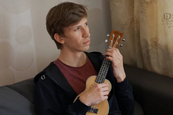 Young blonde guy is playing music on ukulele