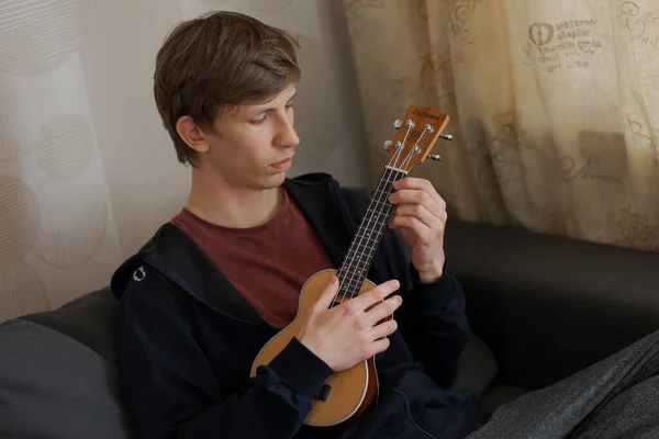 Young blonde guy is playing music on ukulele