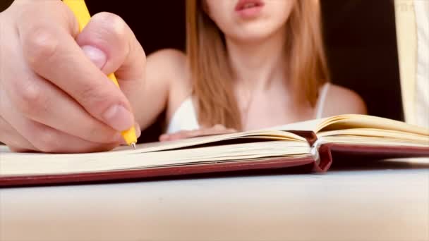 Das blonde Mädchen schreibt mit gelbem Stift in ein Notizbuch. Frauentagebuch. Notizen machen — Stockvideo