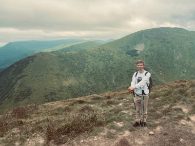 Genç sarışın adam dağlarda. Mavi gökyüzü ve güzel doğa. Formda adam tırman. Yeşil ağaçlar ve yeşil çimenler