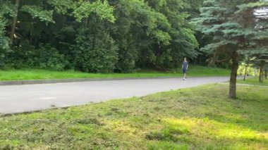 Sarışın yakışıklı adam doğada yürüyor. Yazın adamın etrafında yeşil ağaçlar ve yeşil çimenler. Yakışıklı, formda bir adam yolda yürüyor..