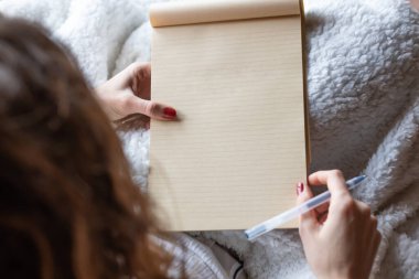 Genç bir kadın evdeki kanepeye elinde kalemle boş bir defterle yazmaya başladı. Defter boş..