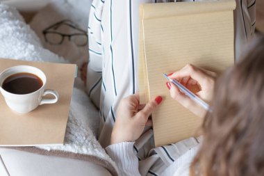 Genç bir kadın evdeki kanepeye elinde kalemle boş bir defterle yazmaya başladı. Defter boş..