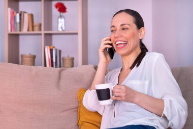 Evdeki kanepede oturmuş akıllı telefondan konuşan güzel ve güzel esmer kadın gülüyor..