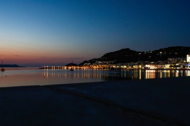 Arkasında köy ışıkları olan bir plajın gün batımı manzarası. Yatay resim.