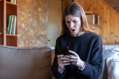 Evdeki kanepede oturan siyah kazaklı, akıllı telefonuyla yazı yazan hoş, esmer bir kadın hayal kırıklığına uğradı.