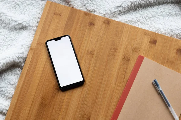 Ahşap bir tahta üzerinde bir defter ve kalem ile boş ekran akıllı telefonunun ayrıntıları. Mobil ekran boş.