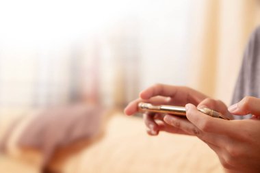 Kadının elini oturma odasının bulanık arka planına karşı cep telefonu kullanarak kapat. Turuncu ton sahnesi. Uzayı kopyala Sosyal uzaklık