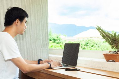 Asyalı erkekler modern ev için bilgisayar ve akıllı telefon kullanıyorlar ve deniyorlar açık hava dağı ve blues arka planı olan, beyaz günlük gömlekler giyiyorlar. Ev konsepti ile çalışmak, fotokopi alanı ile modern ofis kurmak