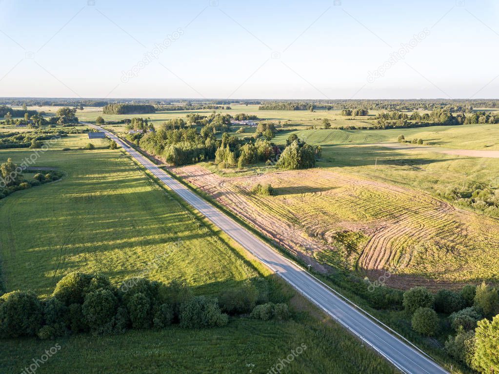 drone image. asphalt road surrounded by pine forest and fields from above in latvia
