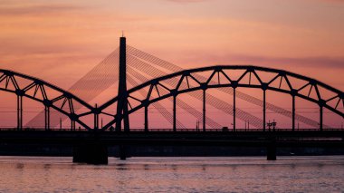 Demiryolu metal köprü siluet nehir, Daugava Riga, Letonya bulutlar ile koyu kırmızı sunet içinde üzerinde