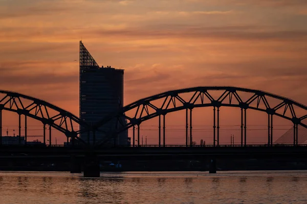 Demiryolu metal köprü siluet nehir, Daugava Riga, Letonya bulutlar ile koyu kırmızı sunet içinde üzerinde