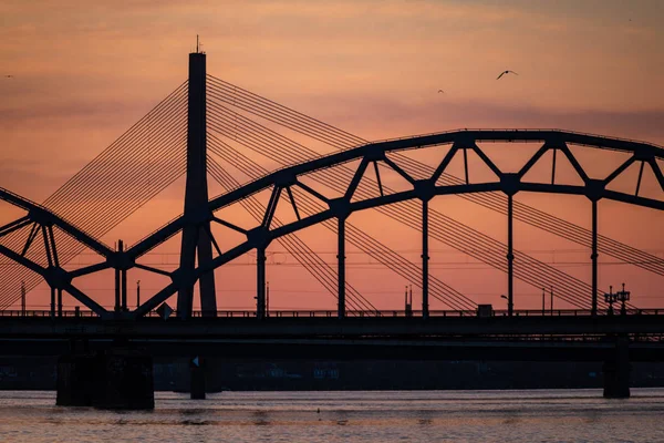 Demiryolu metal köprü siluet nehir, Daugava Riga, Letonya bulutlar ile koyu kırmızı sunet içinde üzerinde