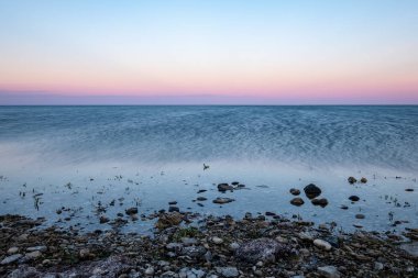 dramatic sunrise over the baltic sea with rocky beach and trees on the shore. long exposure shot. Estonia, Hiiumaa island clipart