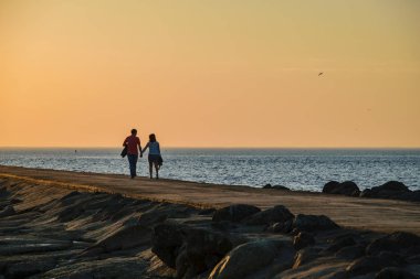 brakewater denizin üzerinde zevk günbatımı insanlar. sıcak yaz gecesi, yürüyüş ve rahatlatıcı anonim kişiler. siluetleri