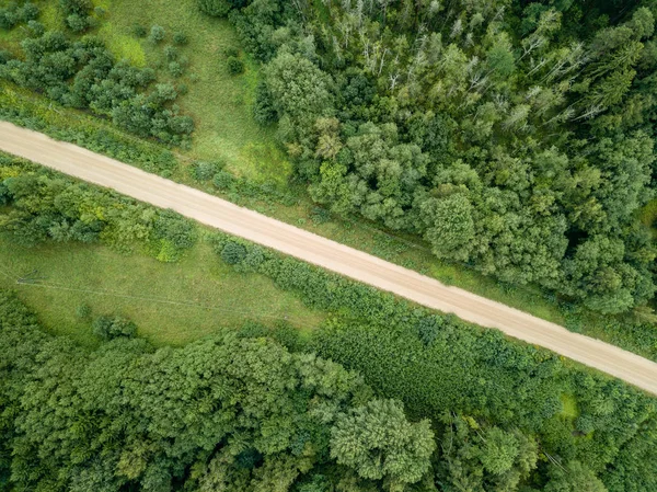 drone görüntü. kırsal çakıl yol yeşil orman ve ağaçları ile yukarıdan gölgelerde güneşli yaz günü hava görünümünü. Letonya