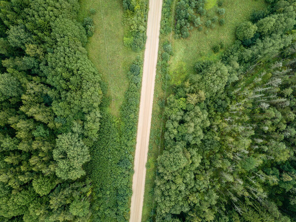 Drone image. aerial view of rural gravel road in green forest and trees with shadows from above in sunny summer day. latvia