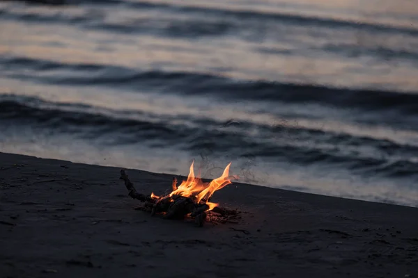 small fire burning on the sea shore at night with waves in background. calm evening