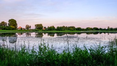 ağaçlar ve ev kıyısında dramatik renkli gökyüzü gün batımında çevrili gölet ile kırsal manzara 