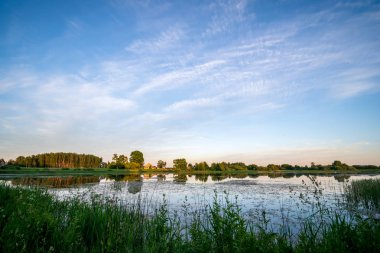 ağaçlar ve ev kıyısında dramatik renkli gökyüzü gün batımında çevrili gölet ile kırsal manzara 