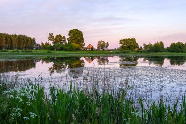 ağaçlar ve ev kıyısında dramatik renkli gökyüzü gün batımında çevrili gölet ile kırsal manzara 