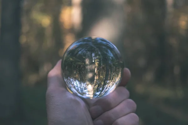 lensball in autumn reflecting nature around it. fall colors hold in human hand - vintage old film look