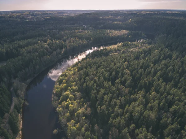 drone image. aerial view of rural area with fields and forests and water reflections in river in cloudy spring day. latvia - vintage old film look