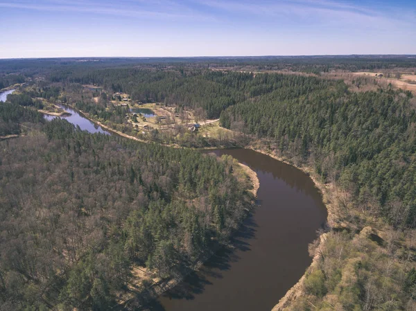 drone image. aerial view of rural area with fields and forests and water reflections in river in cloudy spring day. latvia - vintage old film look