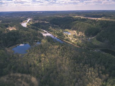 drone görüntü. alanları ve ormanları ve bulutlu bahar günü nehir su yansımalar kırsal alan hava görünümünü. Letonya - vintage eski film bakmak