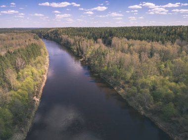 drone görüntü. alanları ve ormanları ve bulutlu bahar günü nehir su yansımalar kırsal alan hava görünümünü. Letonya - vintage eski film bakmak